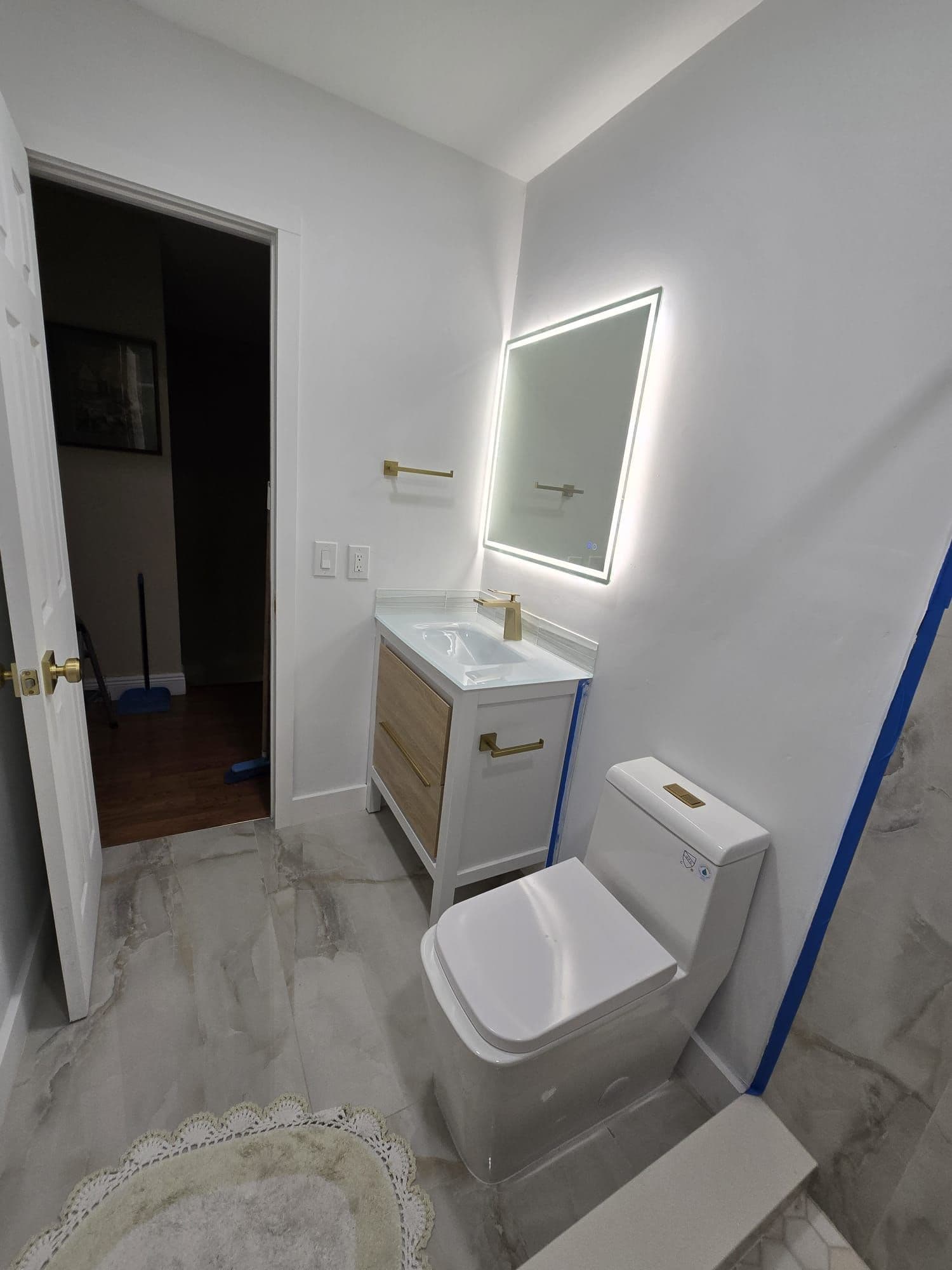 Guest bathroom with a wood vanity, gold fixtures, and marble-look floor tile